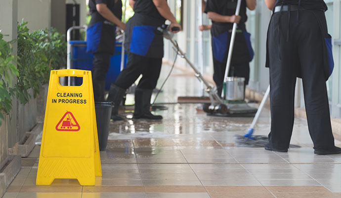 Yellow cleaning in progress sign with janitorial team scrubbing commercial floors