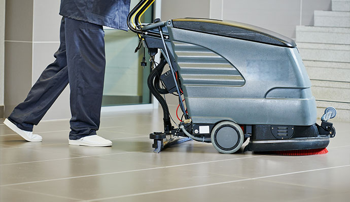Commercial cleaner operating a walk-behind floor scrubber on ceramic tile floor