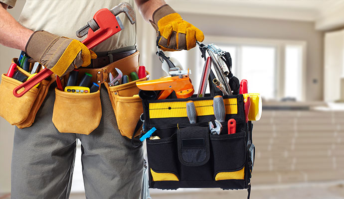 Commercial handyman wearing tool belt and holding full tool bag and pipe wrench