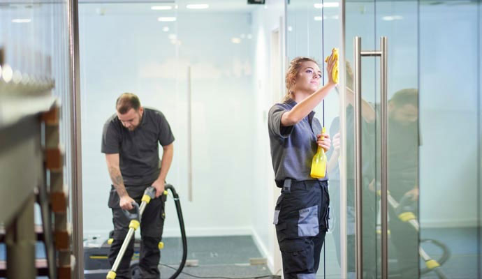 Commercial cleaners vacuuming carpets and wiping glass doors in office building