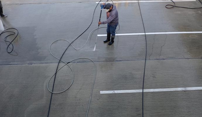 A professional power washing a large concrete commercial parking area