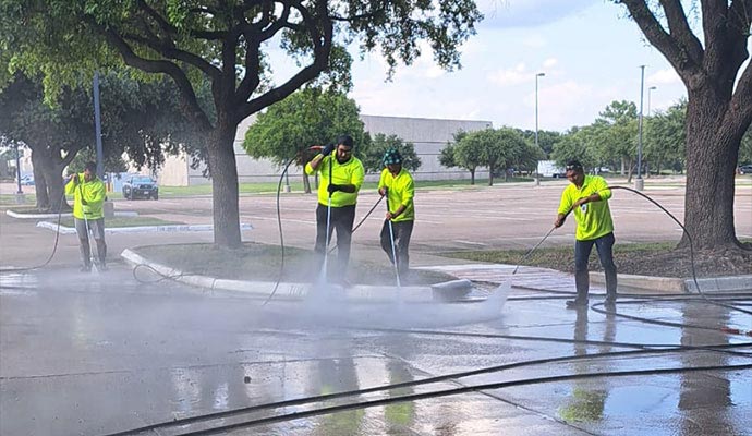 Professional cleaning crew performing commercial pressure washing service on outdoor concrete surfaces and parking areas