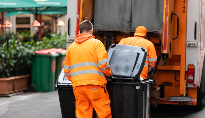 Sanitation workers loading commercial trash bins into waste collection truck