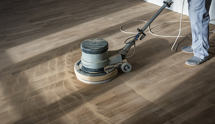 Technician using a floor buffer machine on a dull and scratched wood floor surface