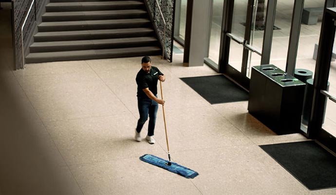 A professional mopping a large stone tile floor in a modern commercial building