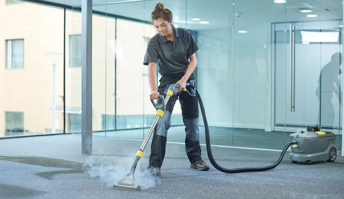 A cleaner uses an industrial carpet cleaning machine with a long hose and wand in a commercial space