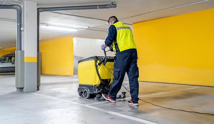 A professional using a floor scrubber-dryer machine to clean a parking garage floor