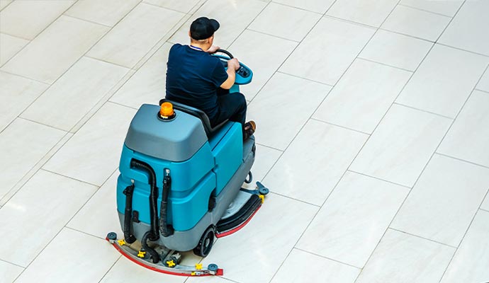 Professional cleaner operating a ride-on floor scrubber to clean a ceramic surface