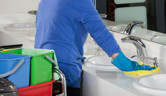 Janitor wiping and sanitizing commercial restroom sink and countertop