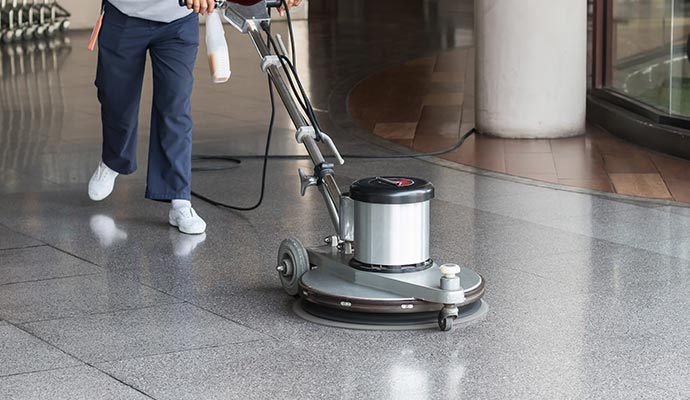 A janitor uses a floor buffer to polish and clean the shiny tile floor of a commercial building