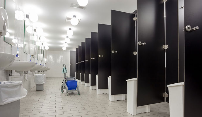 A clean, modern public restroom with a line of sinks, black stalls, and a cleaning cart in the middle of the floor