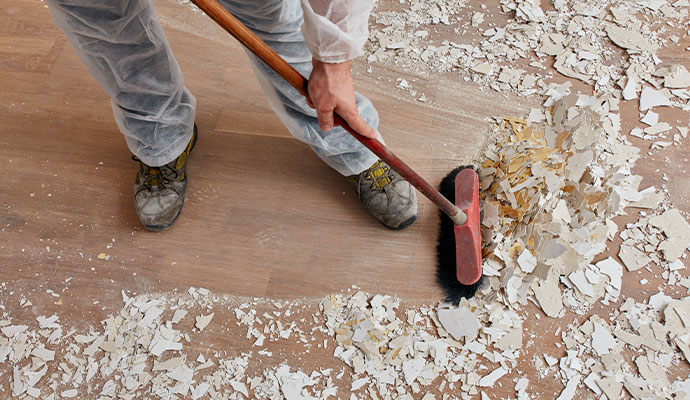 Construction worker sweeping drywall dust and debris from wooden floor during renovation cleanup
