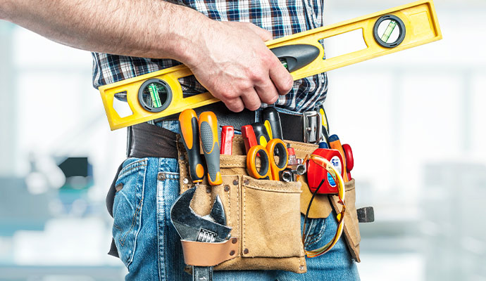 A professional handyman or contractor with a leather tool belt and a yellow level in his hand, ready to work