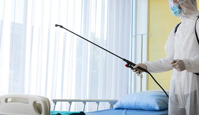 Person wearing full PPE using a sprayer to disinfect and sanitize hospital interiors