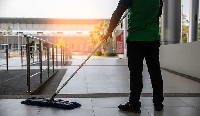 A professional cleaner with a mop cleans the floor of a large, bright commercial building