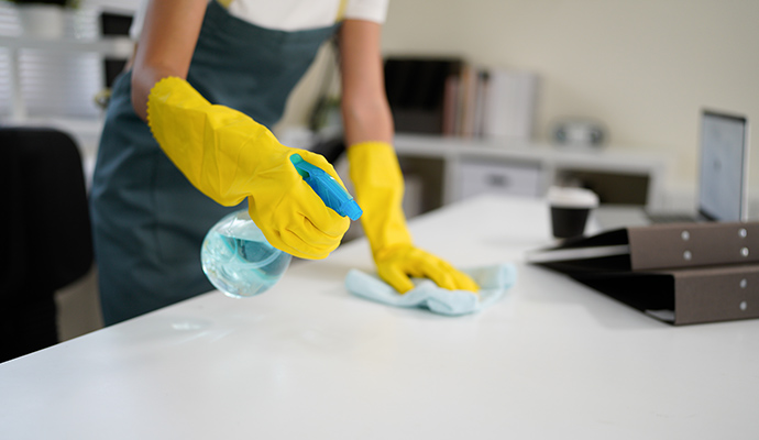 A cleaning professional sanitizing a desk surface in a modern office environment