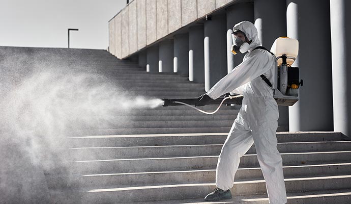 Technician in safety gear applying disinfectant spray to sanitize a commercial area