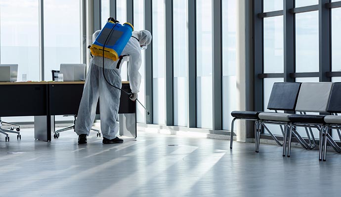 Professional wearing a white protective suit disinfecting the floor and furniture in a modern office space