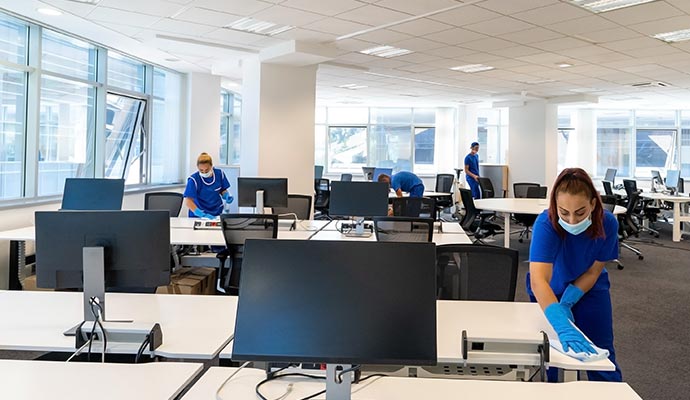Team of professionals cleaning desks and sanitizing surfaces in a modern office