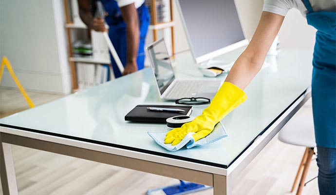 A cleaning professional sanitizing a desk surface in a modern office environment