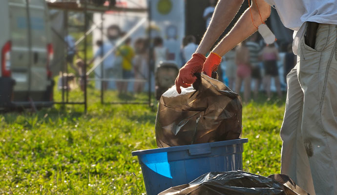 Worker in gloves clearing trash bags during outdoor event cleaning