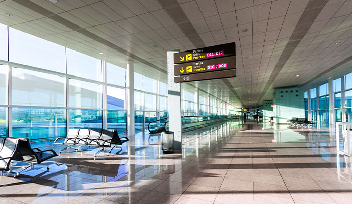A wide shot of a long, clean, and empty airport terminal hallway with large windows, benches, and a sign directing people to gates
