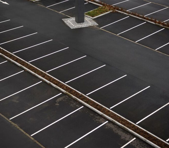 An aerial view of a clean and well-maintained asphalt parking lot with freshly painted white lines and landscaped islands