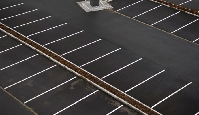An aerial view of a clean and well-maintained asphalt parking lot with freshly painted white lines and landscaped islands