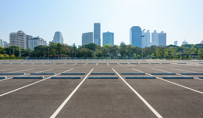 A wide-angle shot of a large, empty commercial parking lot with white painted lines and a backdrop of a modern city skyline