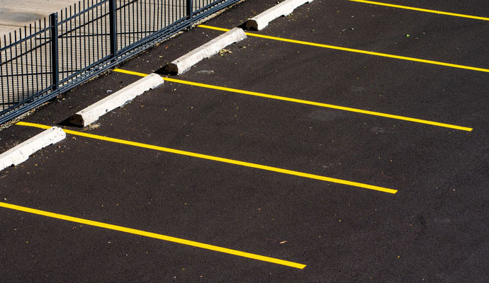 A high-angle view of a clean, empty parking lot with freshly painted bright yellow lines, a metal fence, and concrete car stops