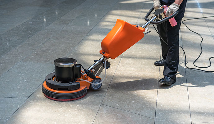 Janitorial worker operating rotary floor buffer on commercial tile floor